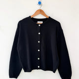 Black cardigan on a wooden hanger against a white background