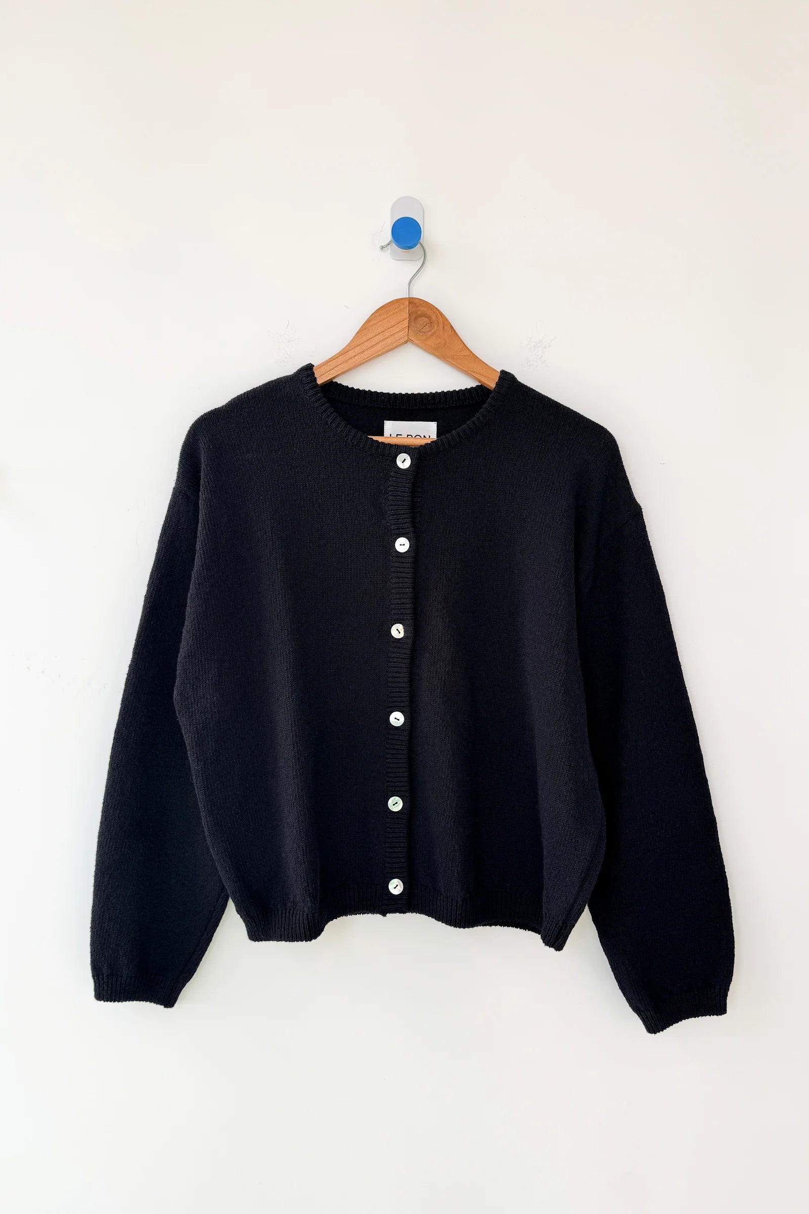 Black cardigan on a wooden hanger against a white background