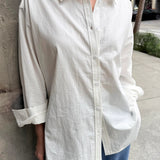 Person wearing a white button-up shirt and blue pants against a stone wall.