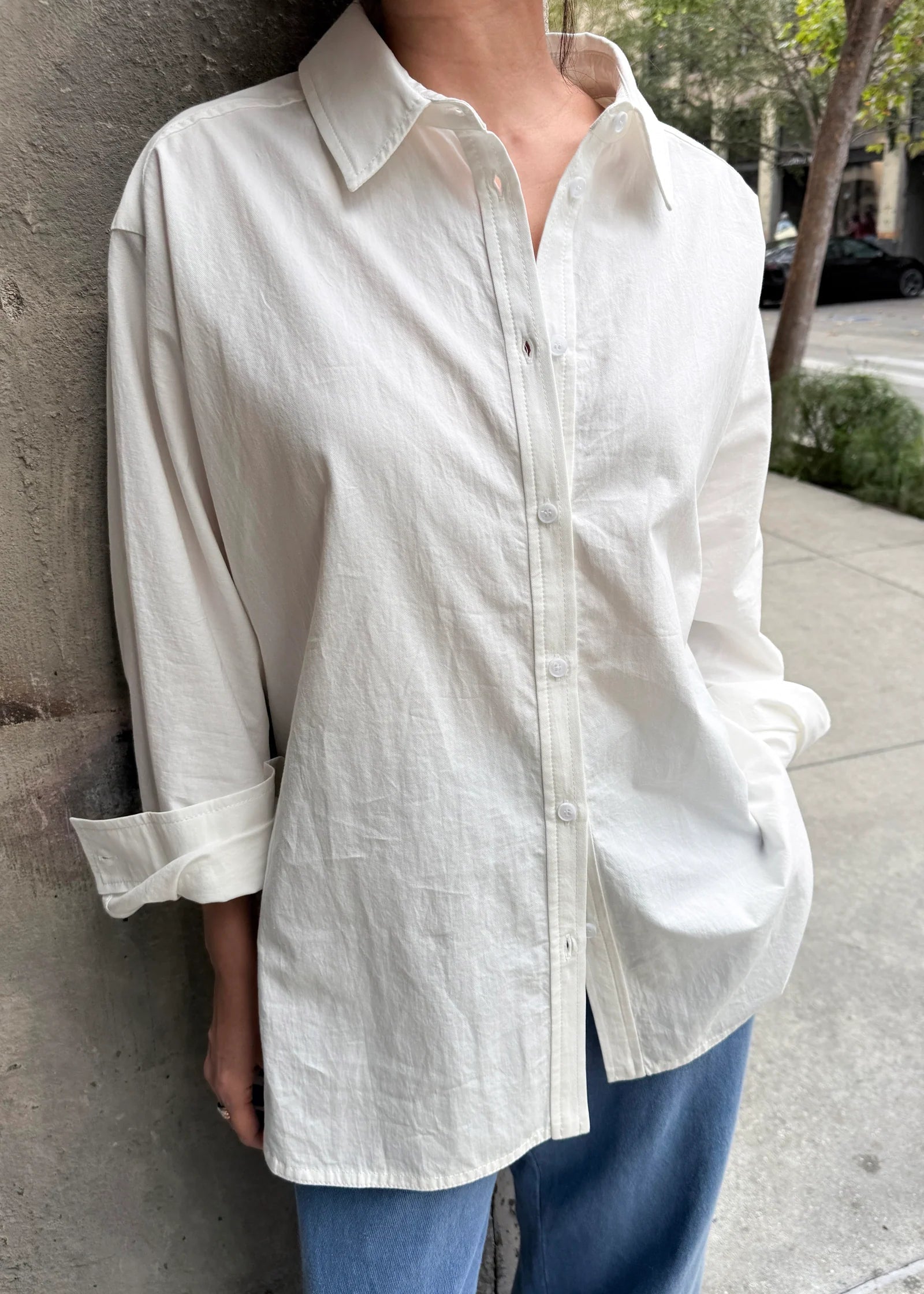 Person wearing a white button-up shirt and blue pants against a stone wall.
