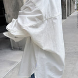 Person wearing a white oversized shirt on a city street.