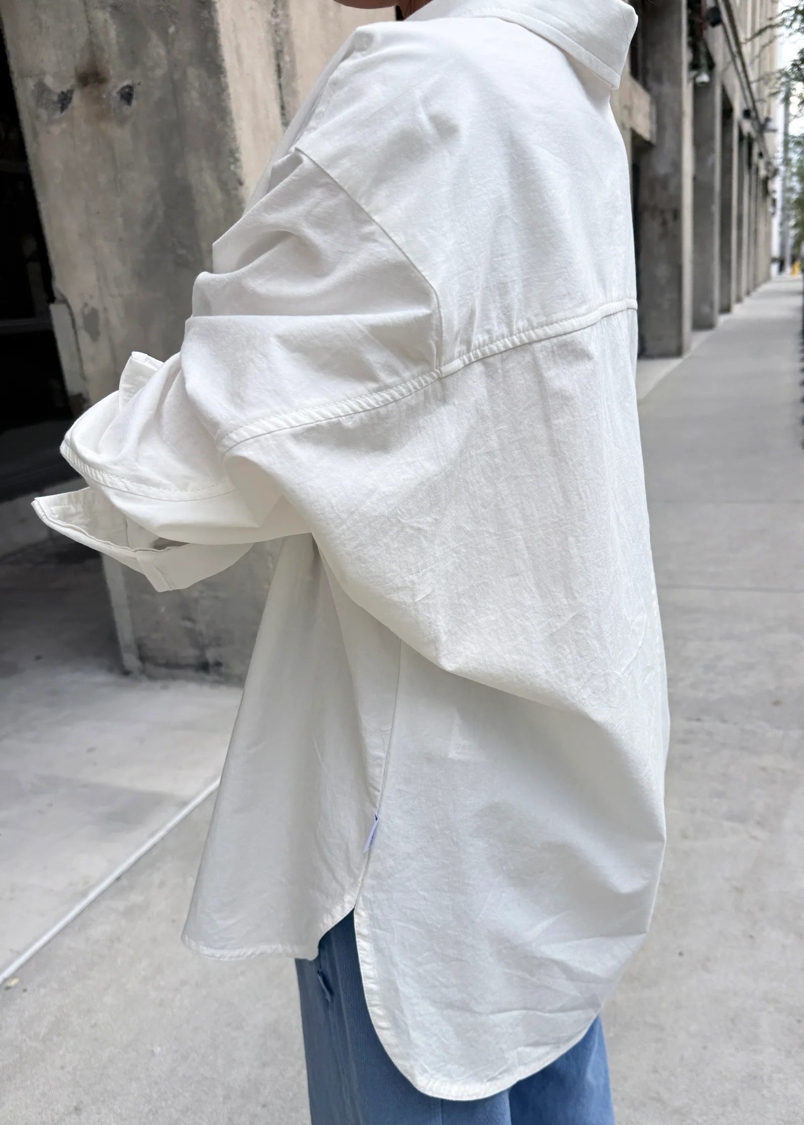Person wearing a white oversized shirt on a city street.