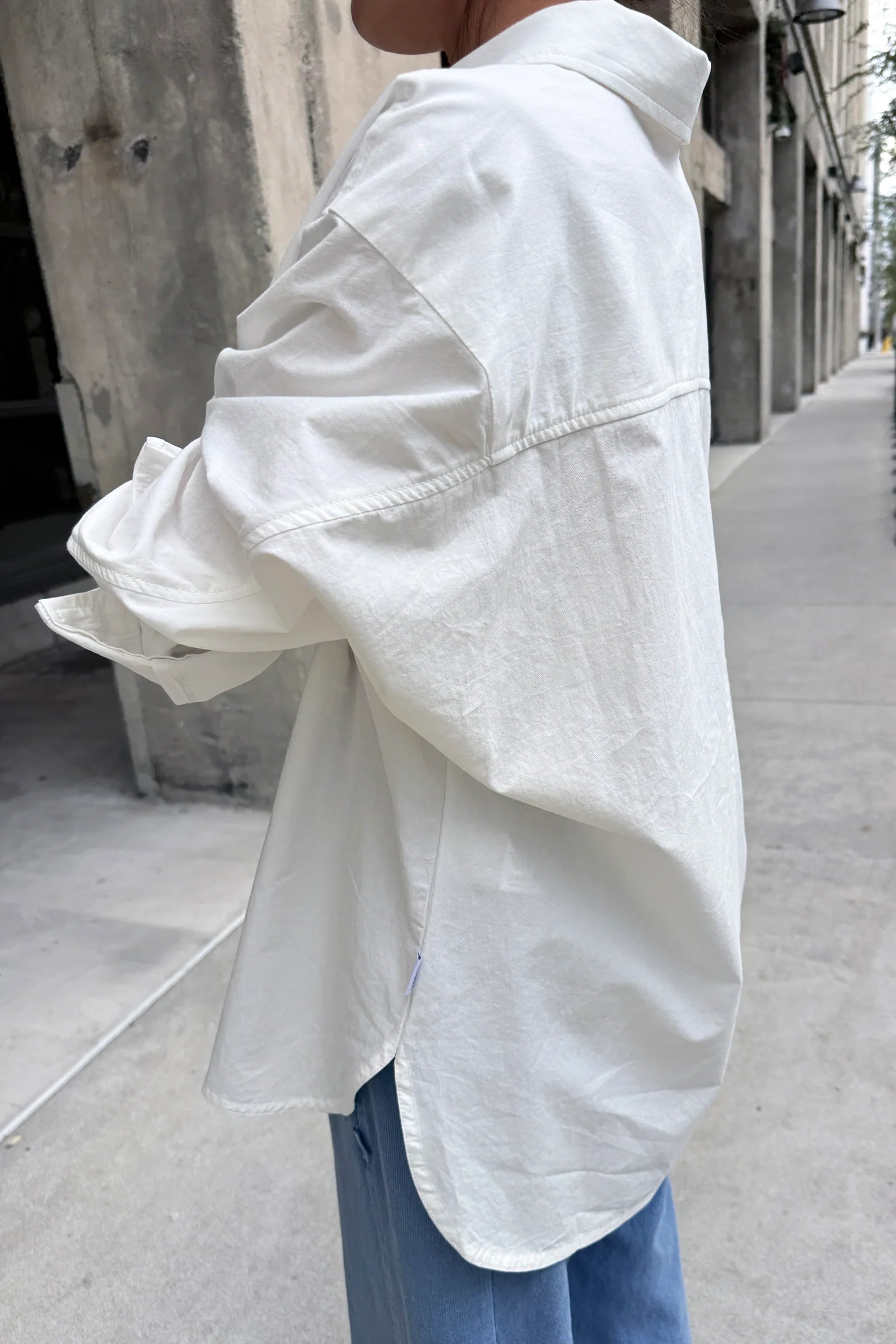 Person wearing a white oversized shirt on a city street.