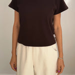Person wearing a black t-shirt and beige pants against a plain background