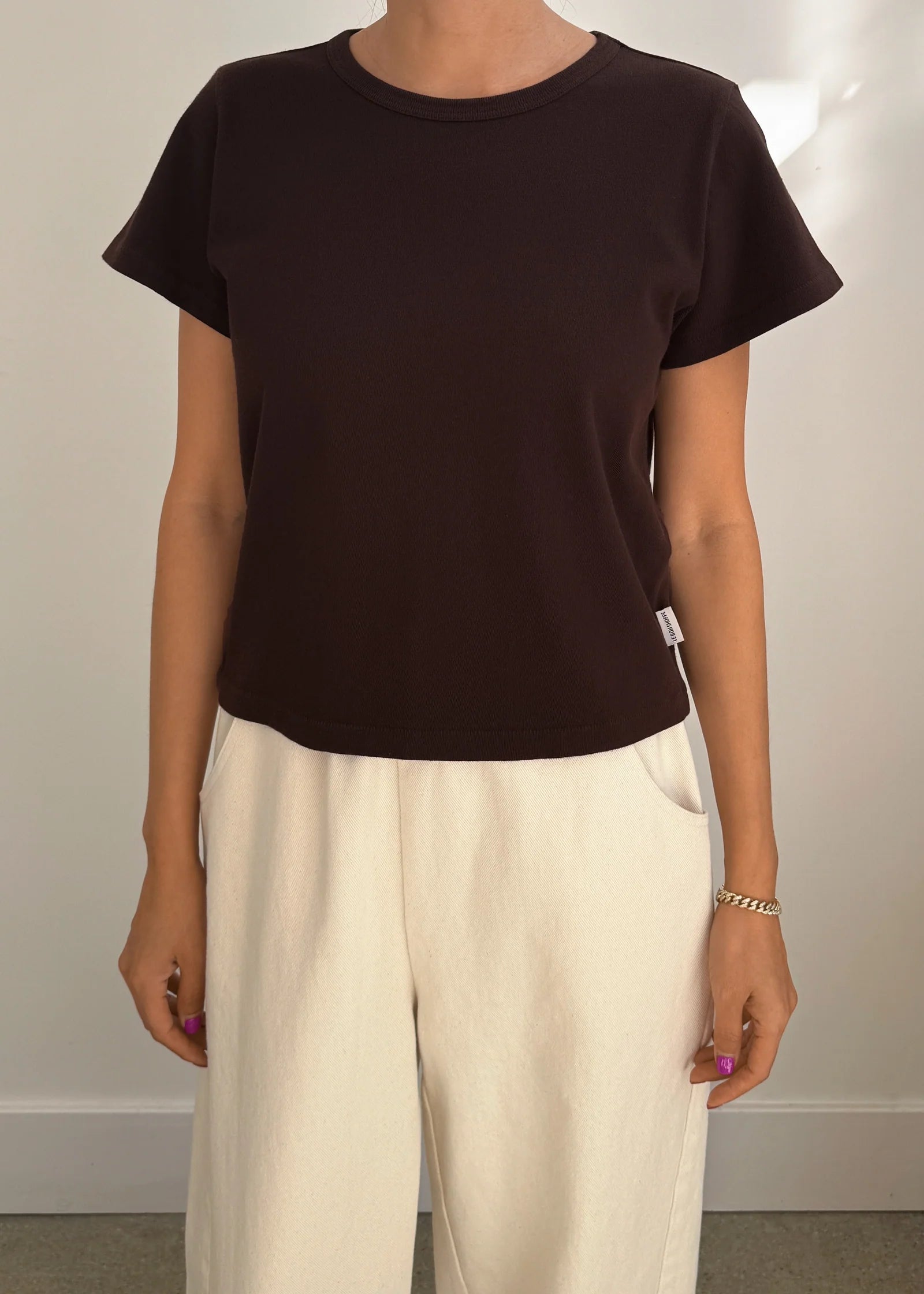 Person wearing a black t-shirt and beige pants against a plain background