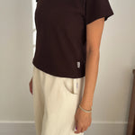 Person wearing a brown t-shirt and beige pants against a plain background