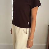 Person wearing a brown t-shirt and beige pants against a plain background