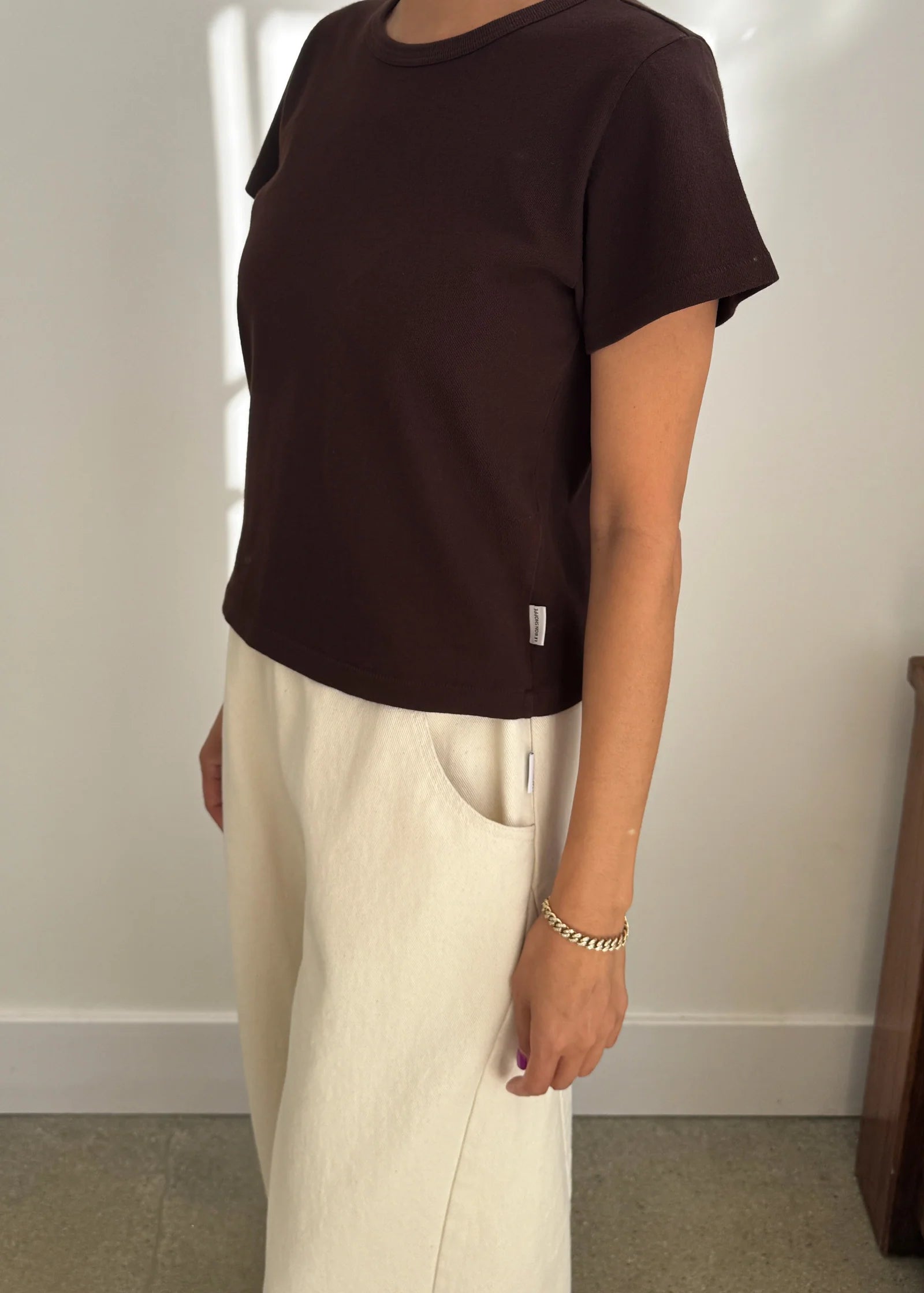 Person wearing a brown t-shirt and beige pants against a plain background