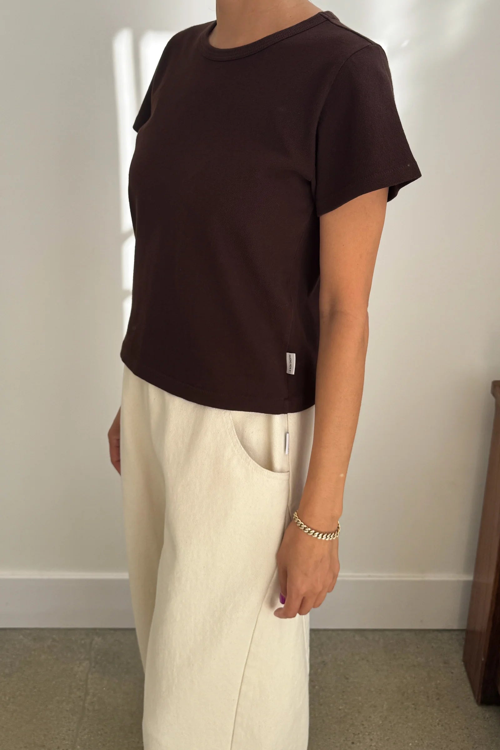Person wearing a brown t-shirt and beige pants against a plain background