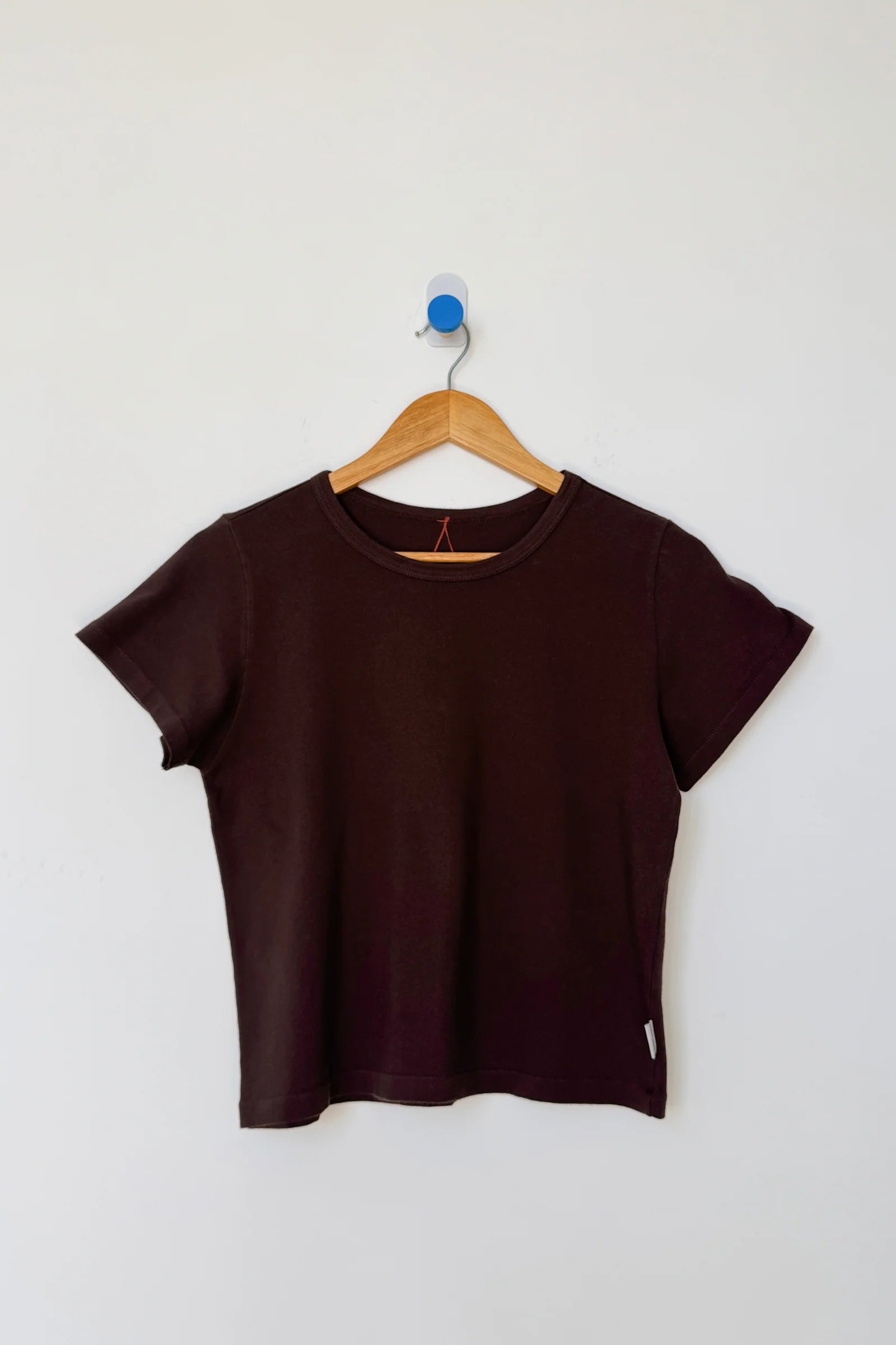 Brown t-shirt on a wooden hanger against a white wall