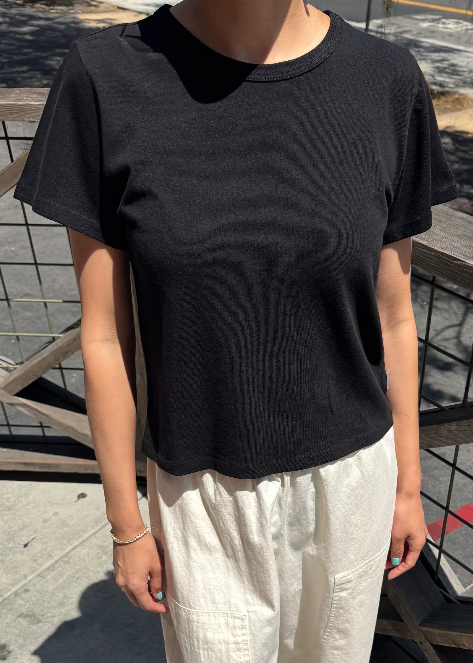 Person wearing a black t-shirt and white pants standing outdoors.