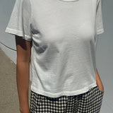 Person wearing a plain white t-shirt and checkered pants against a gray background