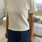 Person wearing a white t-shirt and blue jeans in a room with a couch and plant.