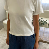 Person wearing a white t-shirt and blue jeans in a room with a couch and plant.