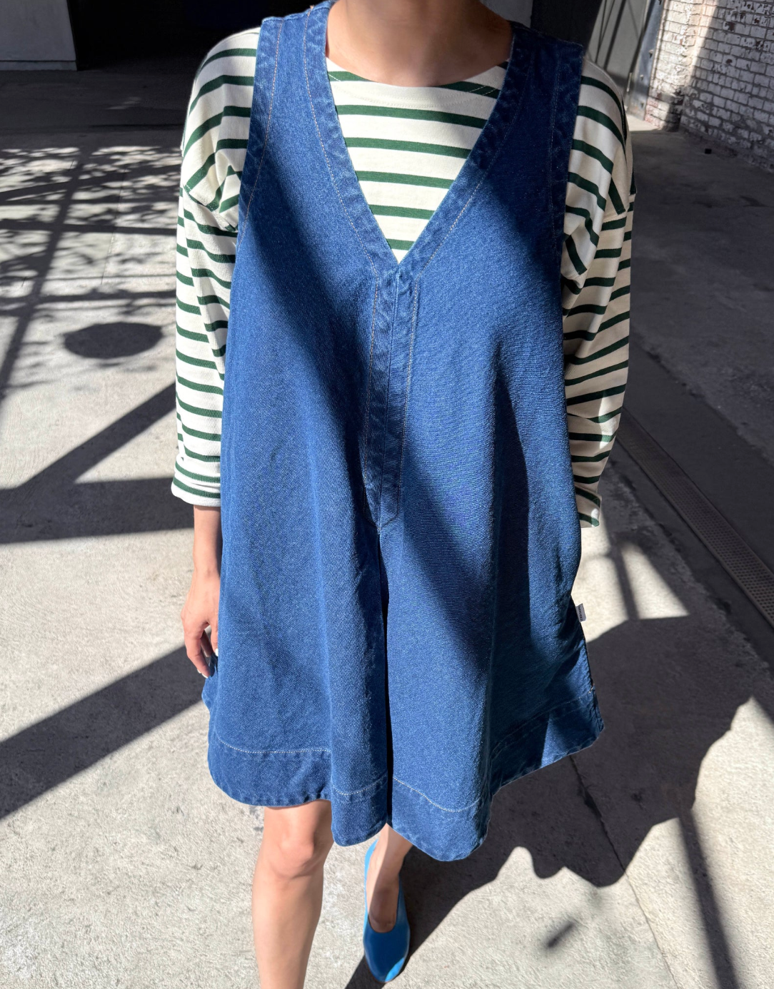 Person wearing a blue denim vest over a striped shirt on a concrete surface.