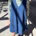 Person wearing a blue denim vest over a striped shirt on a concrete surface.