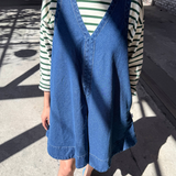Person wearing a blue denim vest over a striped shirt on a concrete surface.
