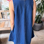 Person wearing a blue denim dress in an outdoor setting with plants and a wooden bench.