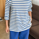 Person wearing a blue and white striped shirt and blue pants in a room with a couch and window.