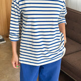 Person wearing a blue and white striped shirt and blue pants in a room with a couch and window.
