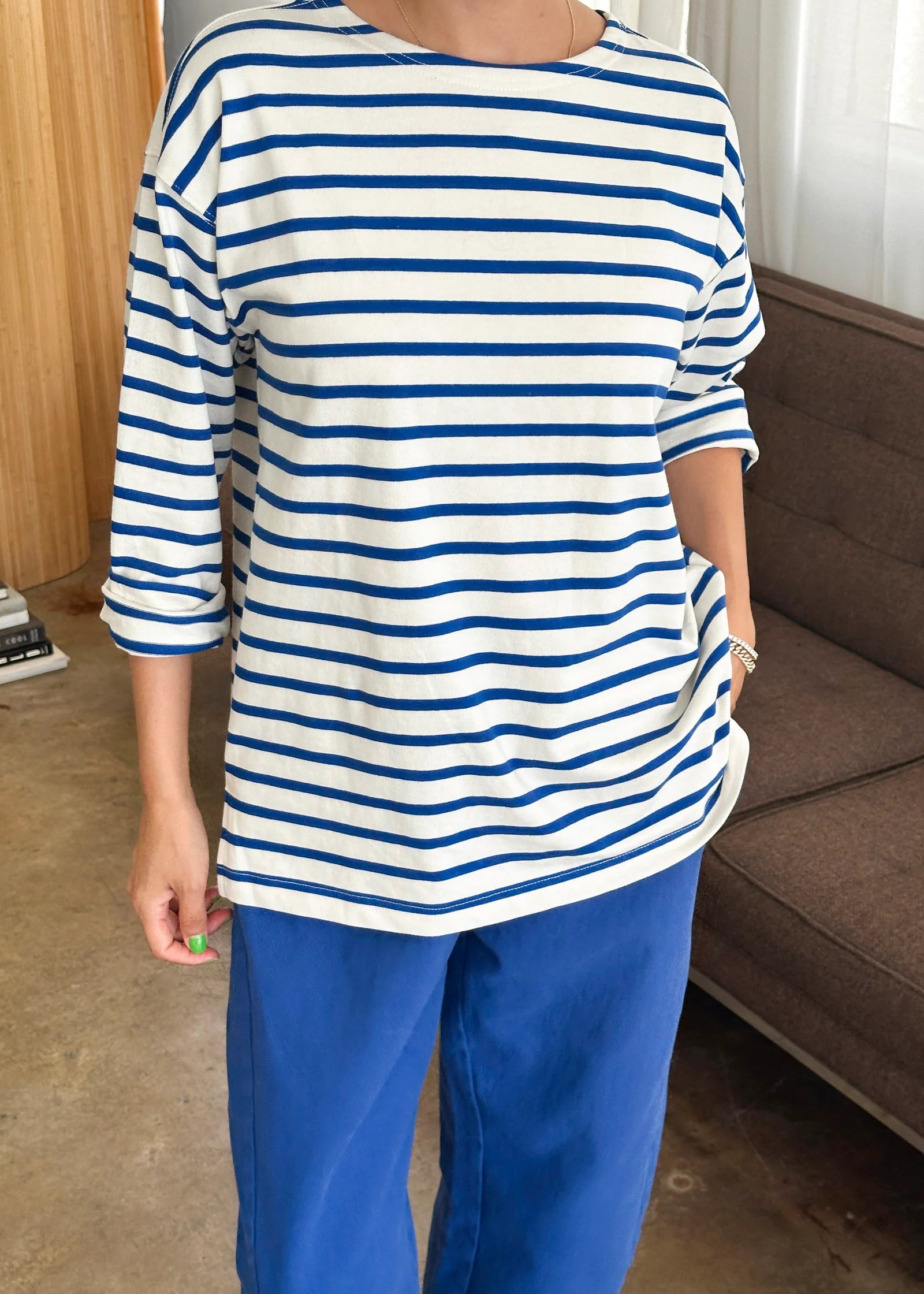 Person wearing a blue and white striped shirt and blue pants in a room with a couch and window.