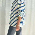 Person wearing a blue and white striped shirt with rolled-up sleeves, standing against a white curtain.