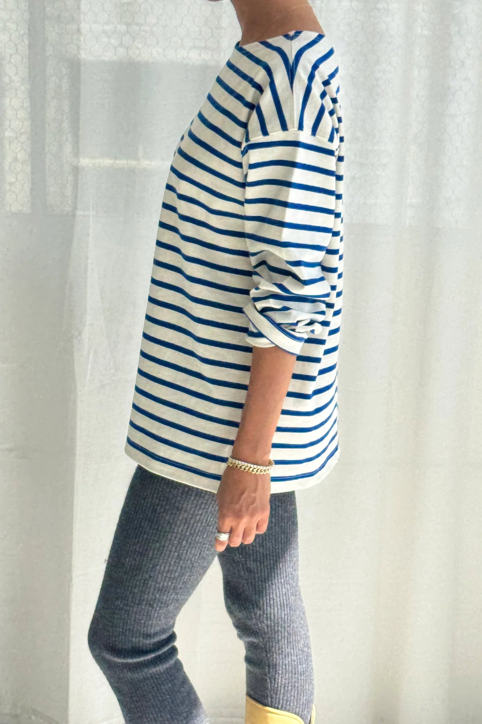 Person wearing a blue and white striped shirt with rolled-up sleeves, standing against a white curtain.