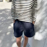 Person wearing a navy and white striped shirt with navy shorts standing against a light-colored wall.