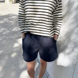 Person wearing a navy and white striped shirt with navy shorts standing against a light-colored wall.