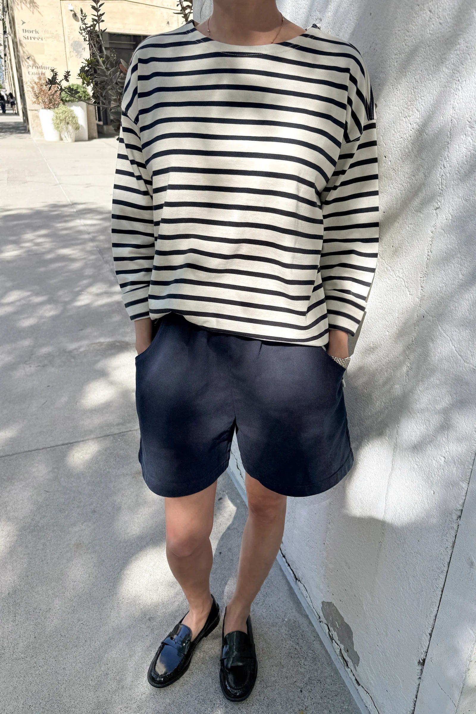 Person wearing a navy and white striped shirt with navy shorts standing against a light-colored wall.