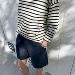 Person wearing a navy and white striped sweater and navy shorts against a light gray wall.