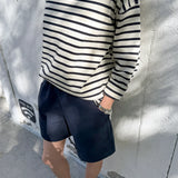 Person wearing a navy and white striped sweater and navy shorts against a light gray wall.