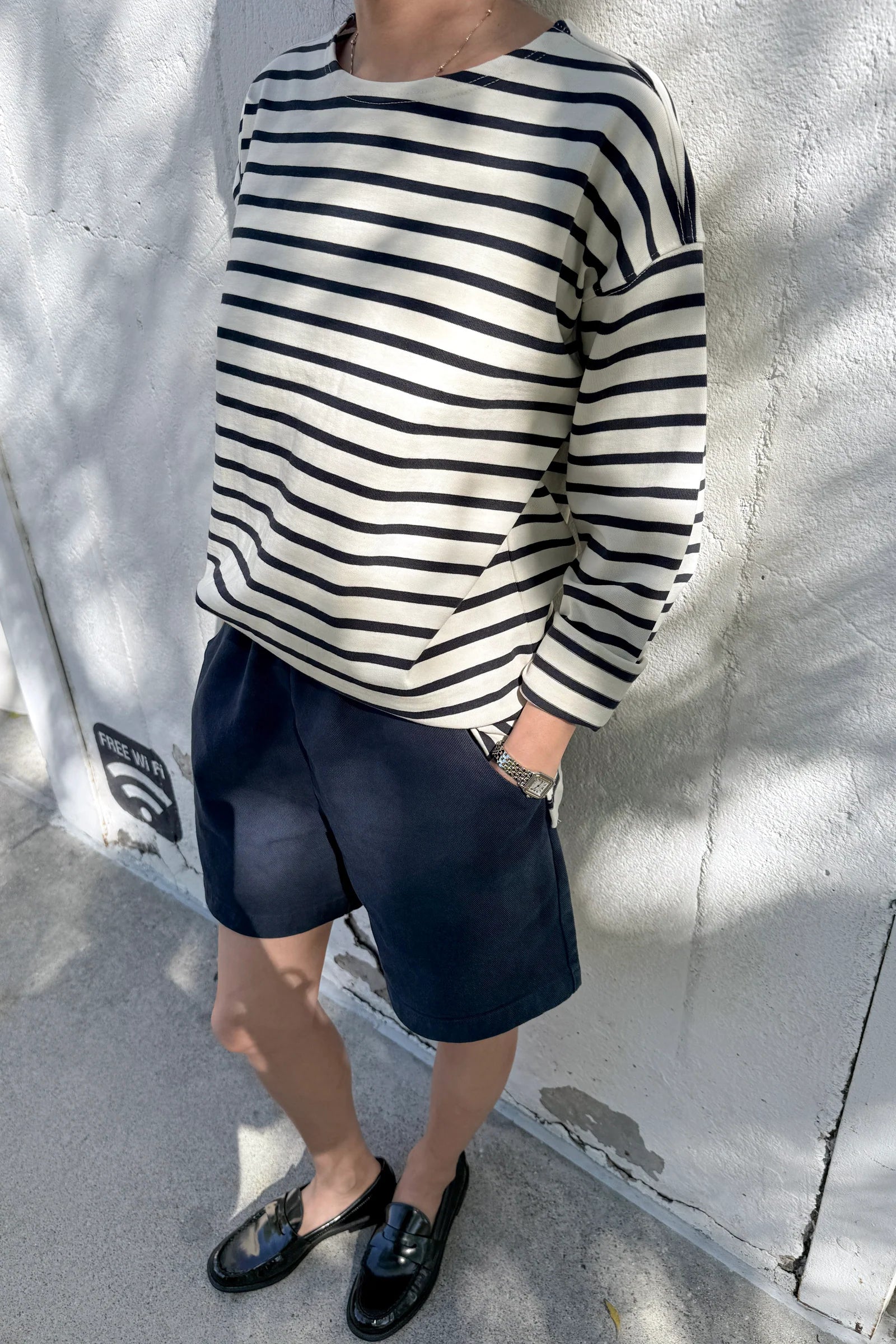 Person wearing a navy and white striped sweater and navy shorts against a light gray wall.