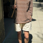 Person wearing a brown and white striped shirt with beige shorts on a sidewalk.