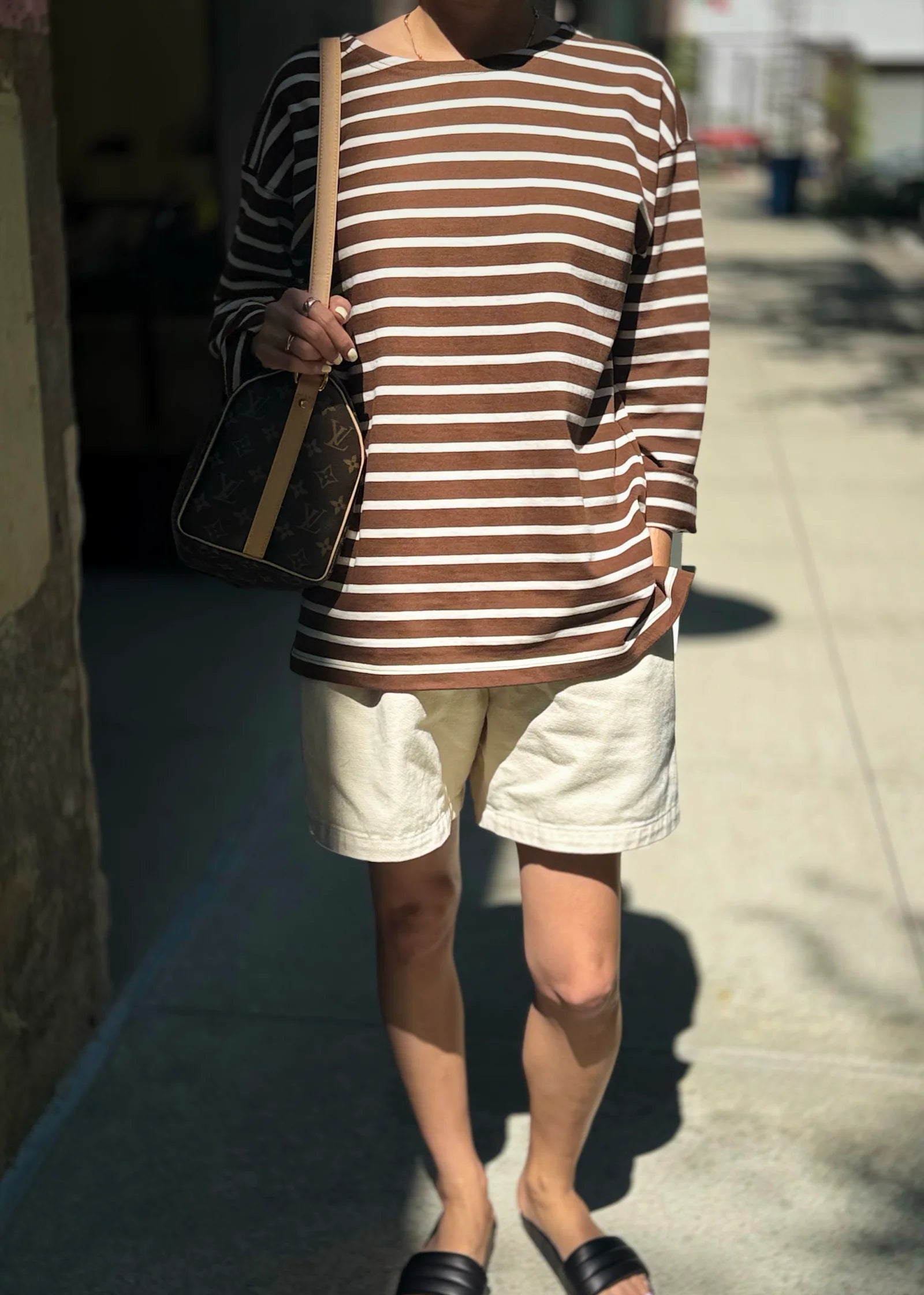 Person wearing a brown and white striped shirt with beige shorts on a sidewalk.