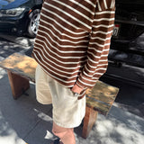 Person wearing a brown and white striped shirt and beige shorts standing on a sidewalk with cars in the background.