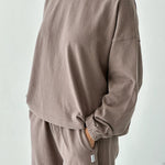 Person wearing a brown sweatshirt and pants set against a white background