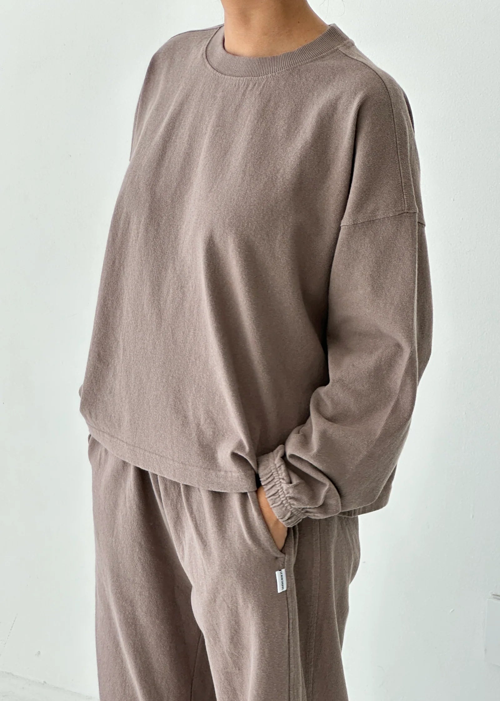 Person wearing a brown sweatshirt and pants set against a white background