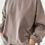Person wearing a brown sweatshirt and pants on a white background