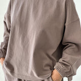 Person wearing a brown sweatshirt and pants on a white background