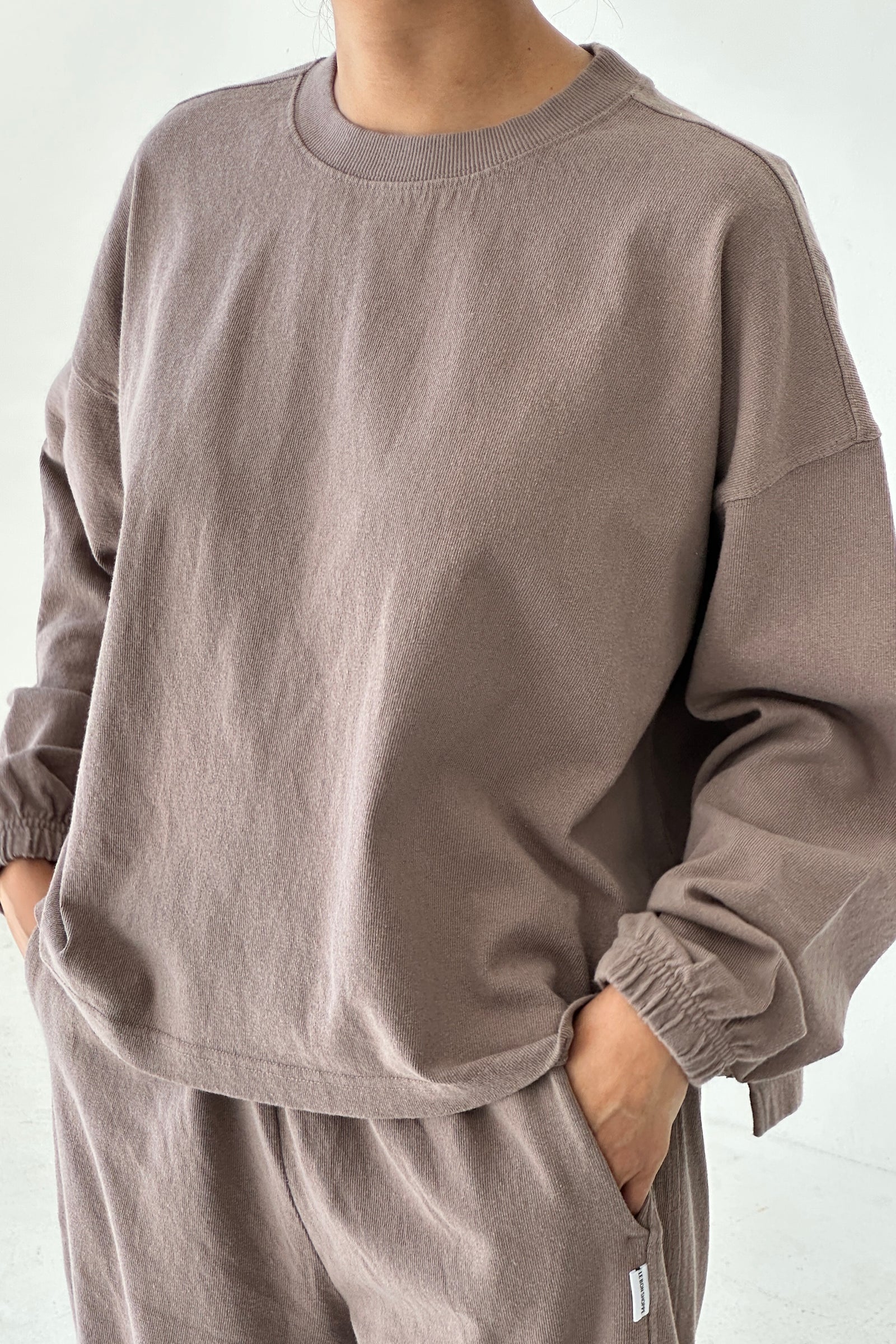 Person wearing a brown sweatshirt and pants on a white background