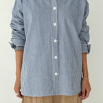 Person wearing a blue and white striped shirt with rolled-up sleeves on a plain background