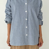 Person wearing a blue and white striped shirt with rolled-up sleeves on a plain background