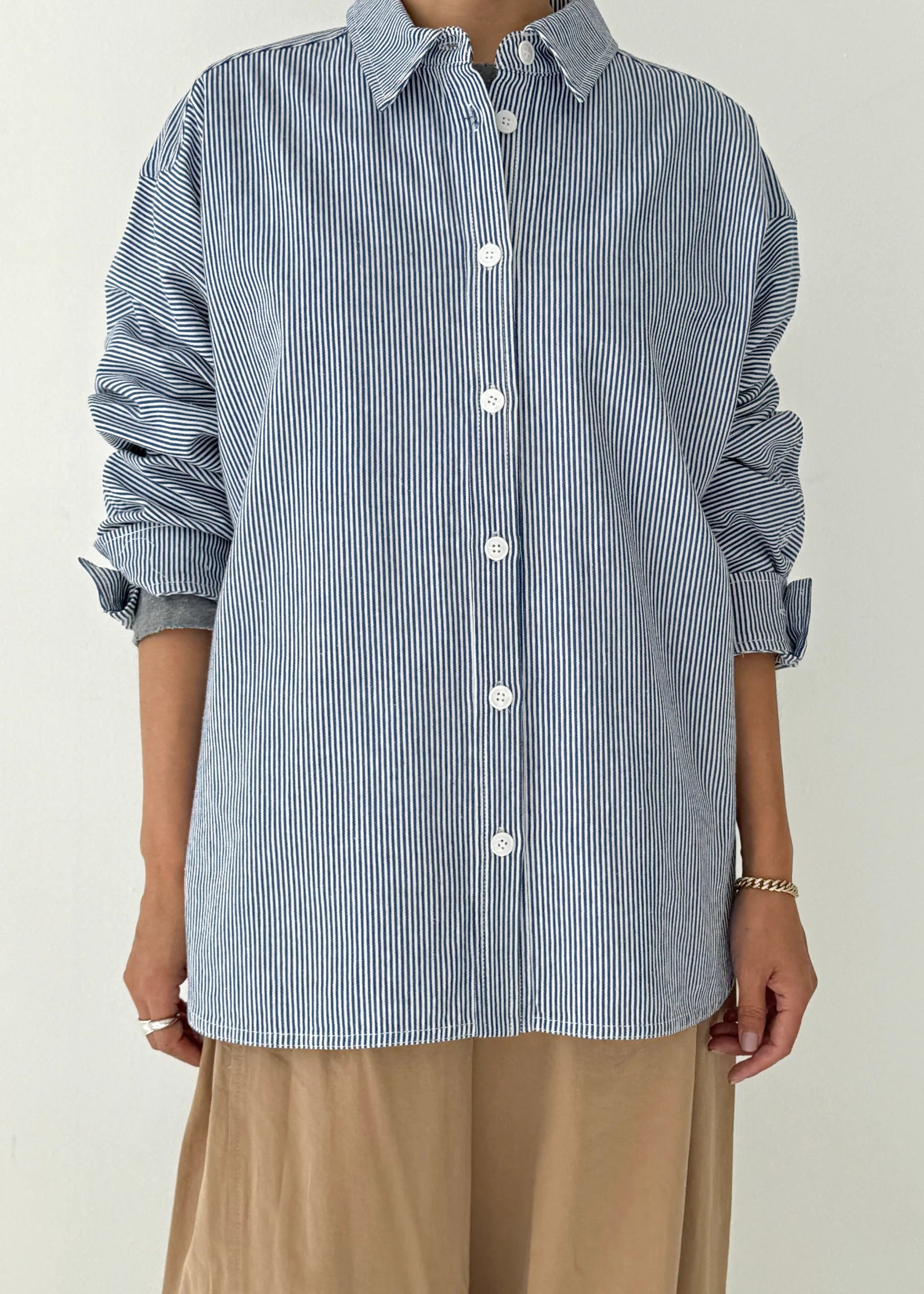 Person wearing a blue and white striped shirt with rolled-up sleeves on a plain background