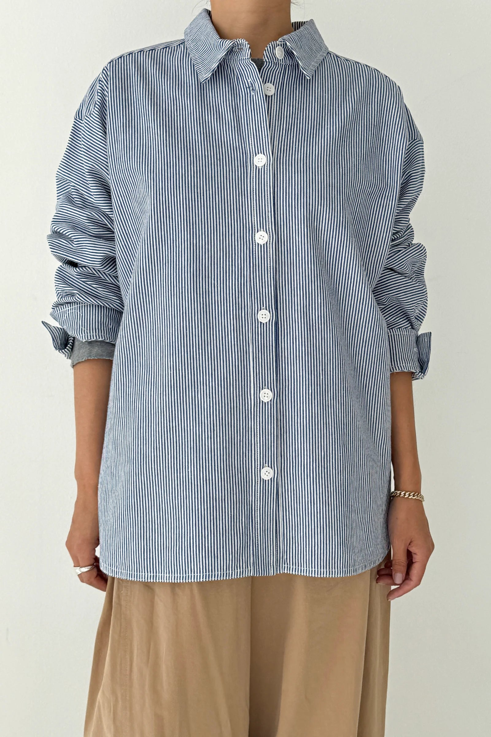Person wearing a blue and white striped shirt with rolled-up sleeves on a plain background
