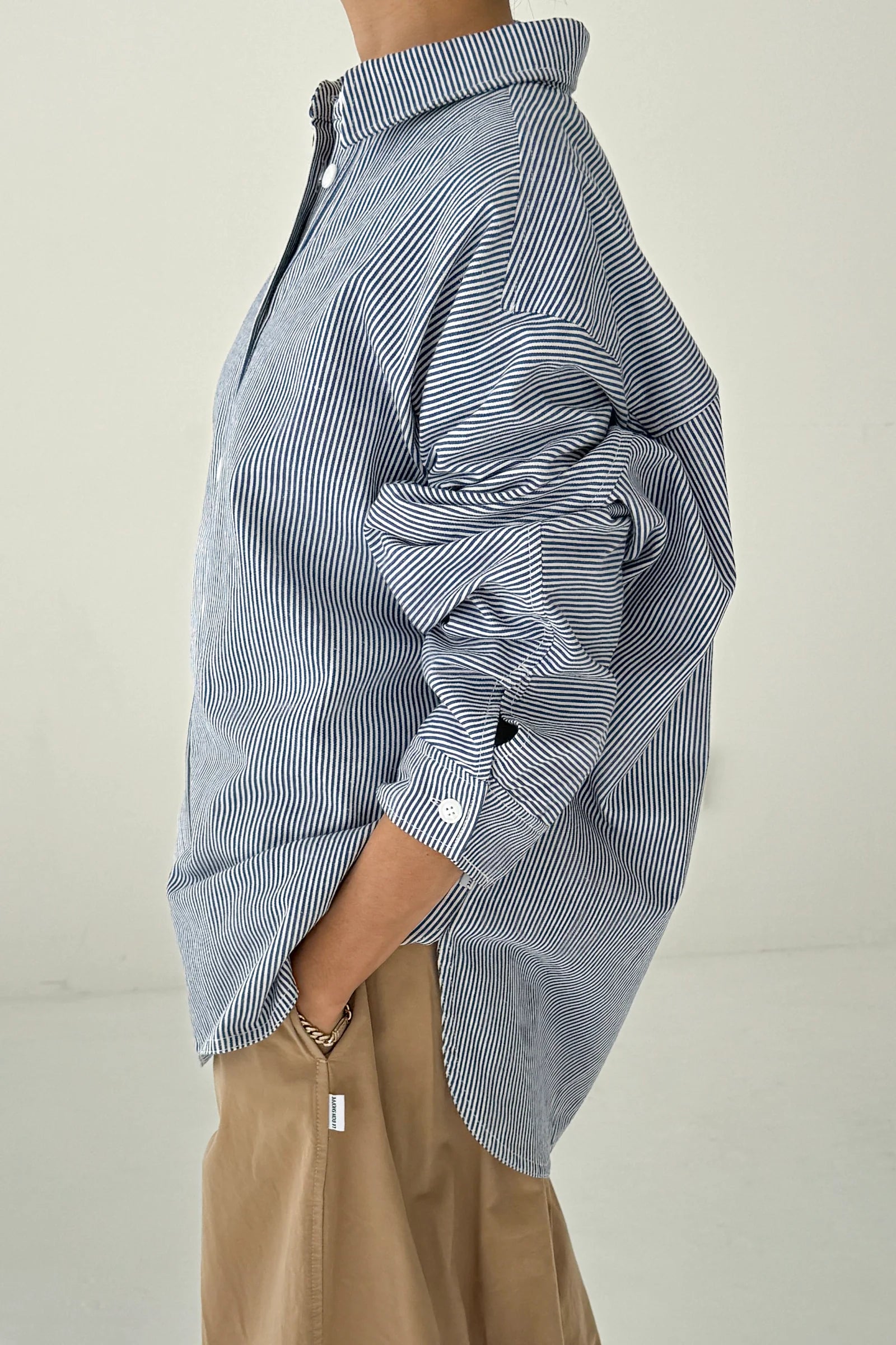 Person wearing a blue and white striped shirt with rolled-up sleeves on a plain background