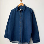Dark denim button up shirt on a wood hanger with a white background