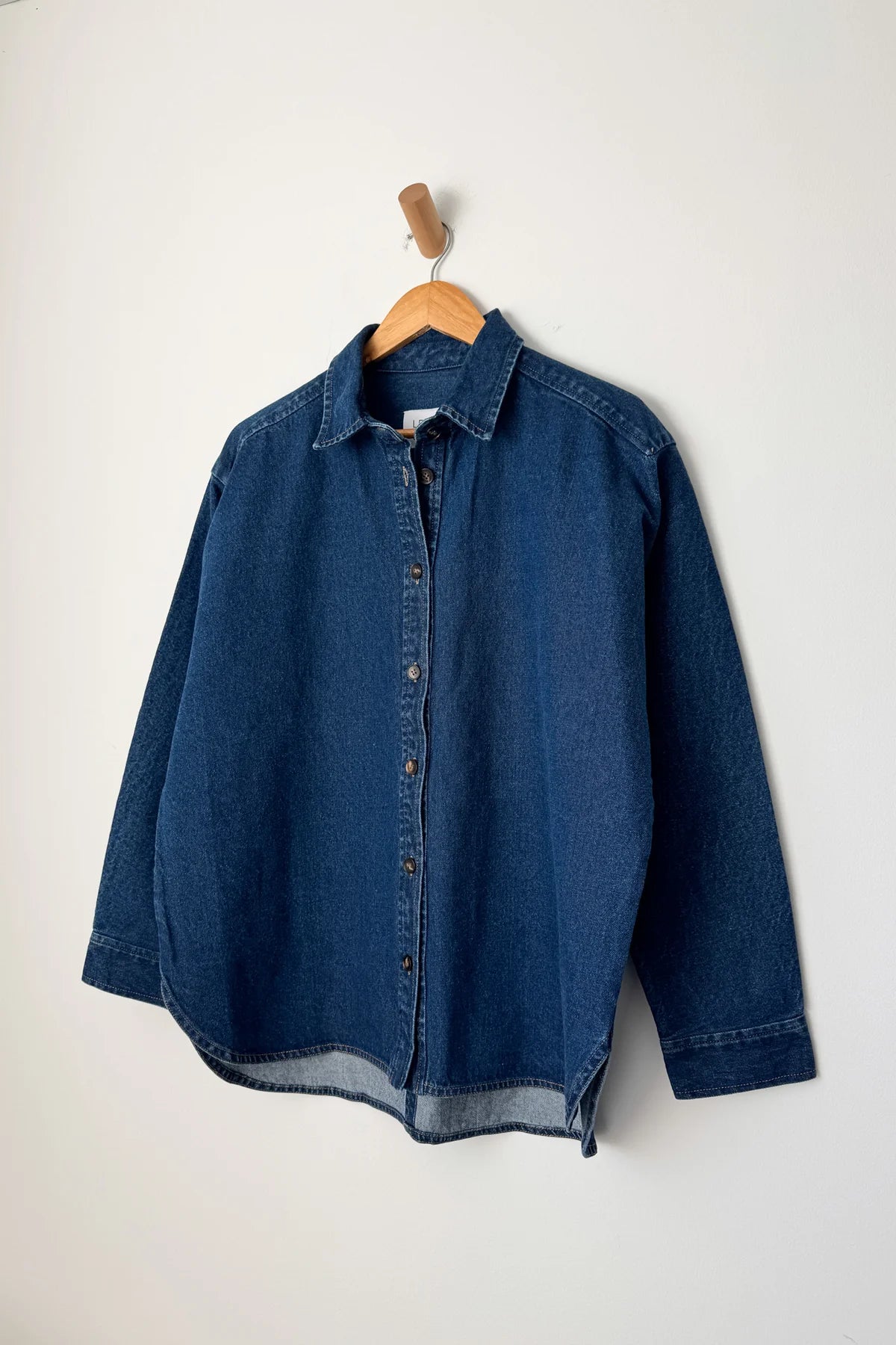 Dark denim button up shirt on a wood hanger with a white background