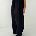 Person wearing black wide-leg pants and a brown top on a white background