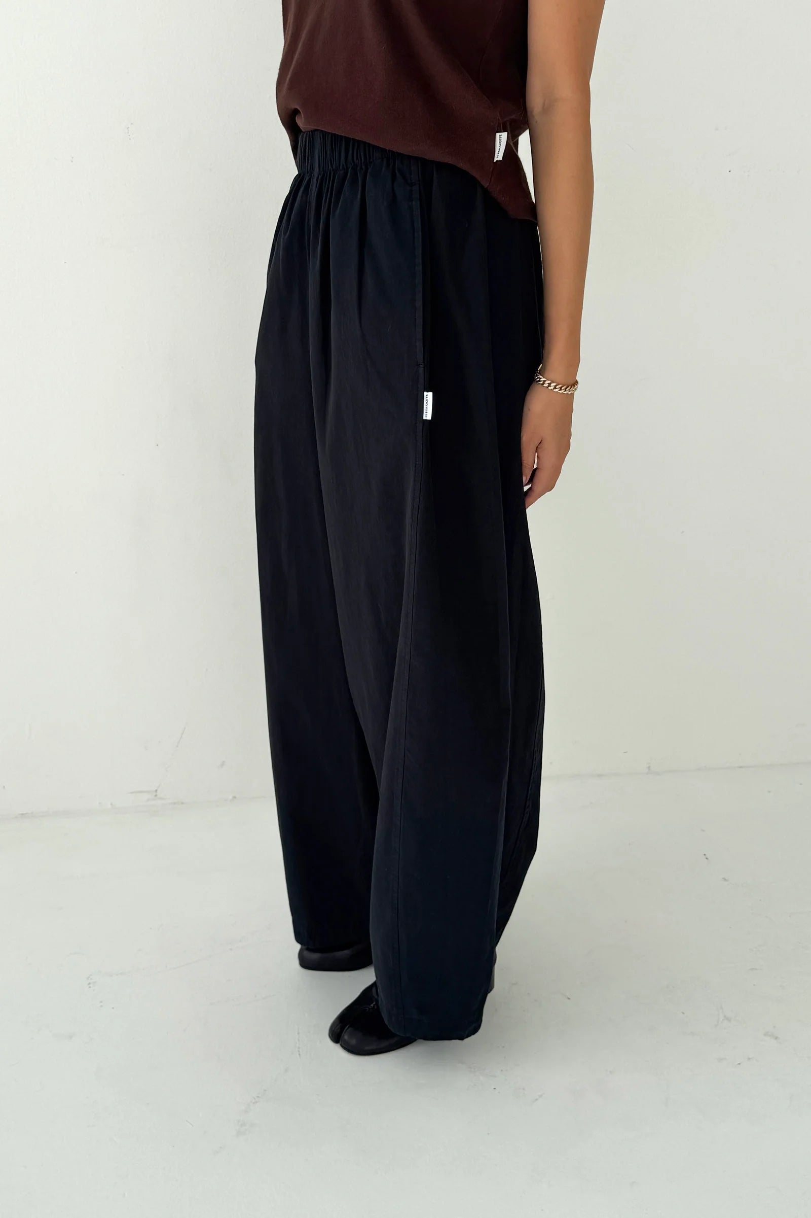 Person wearing black wide-leg pants and a brown top on a white background